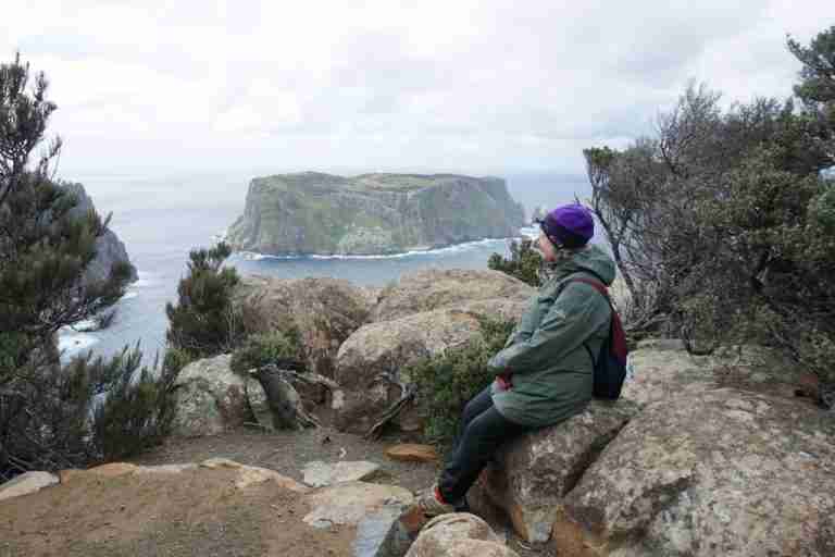 solo travel Tasmania sitting on a rock enjoying the island and water views on the three capes track, the perfect hike for a 10 days in Tasmania itinerary