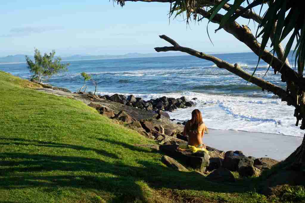 a girl in a bikini sitting on the beach in Byron Bay in Australia