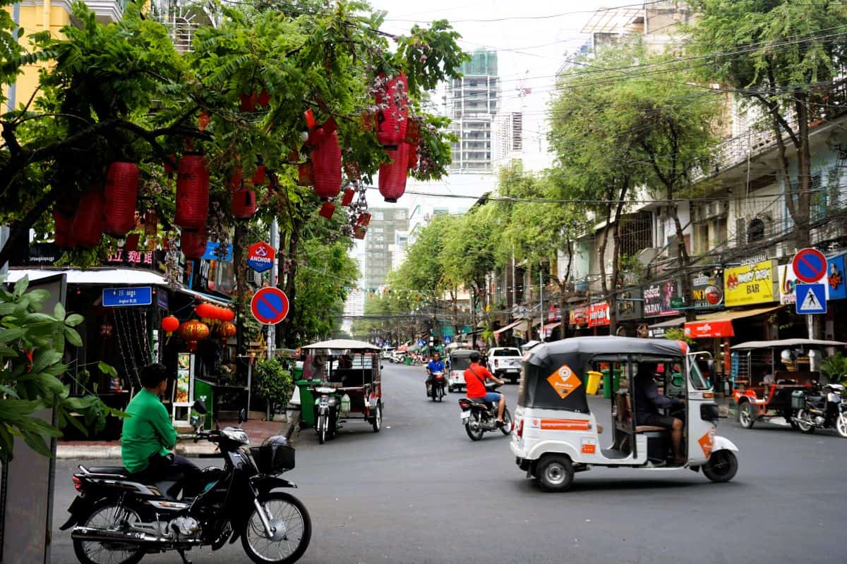 Tuk-tuks and motors bikes on the busy treelined streets of Phnom Penh in Cambodia