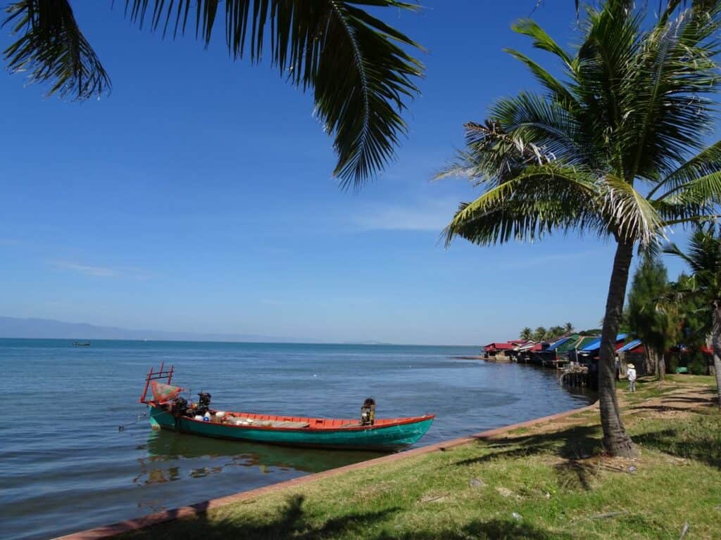 A longtail boat moored near Palm trees and grass in Kep Cambodia