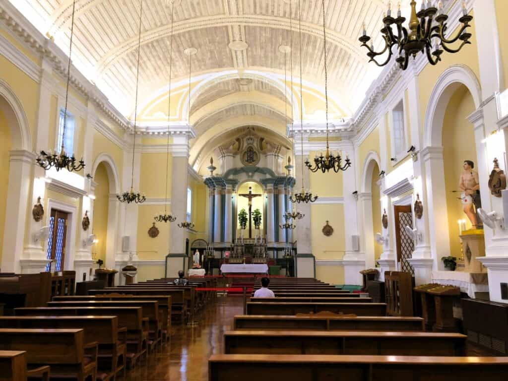 Wooden church pews and a pastel yellow walls inside the St Anthony's Church in Macau
