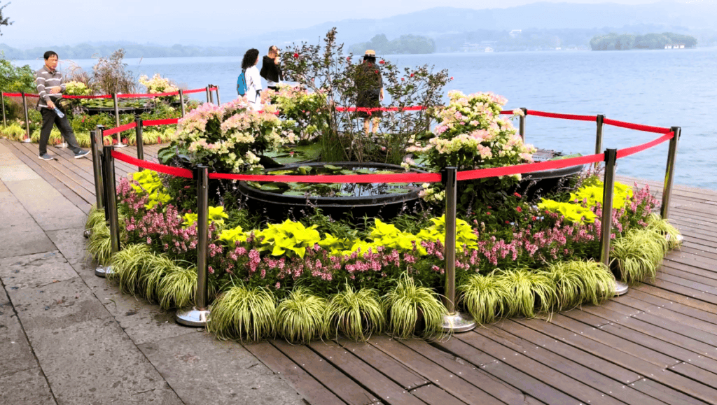 people enjoying the view of a lake beside a colourful flower bed