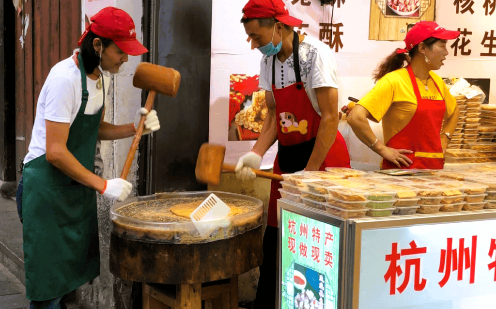 2 men wearing red hats and aprons making traditional Chinese sweets 