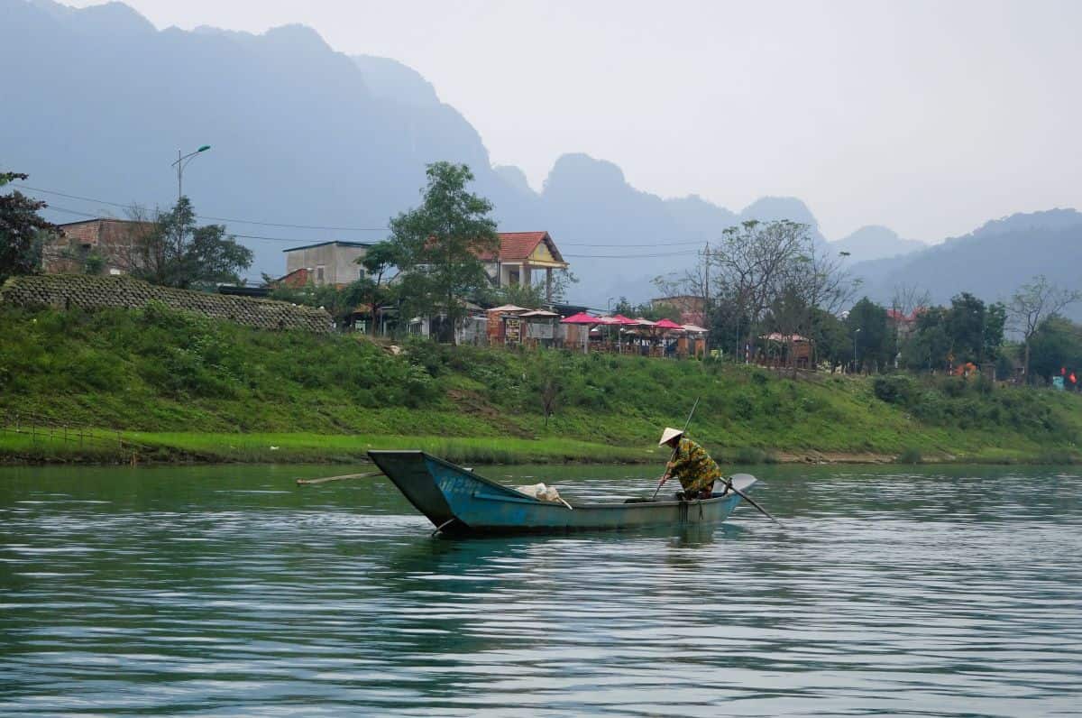 boat on a river with green grassy banks and tall mountains behind