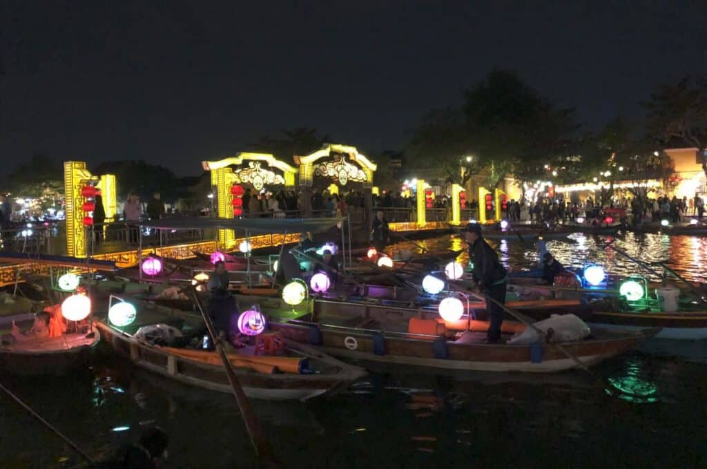 night time rowboats lit with lanterns on the river with lights behind