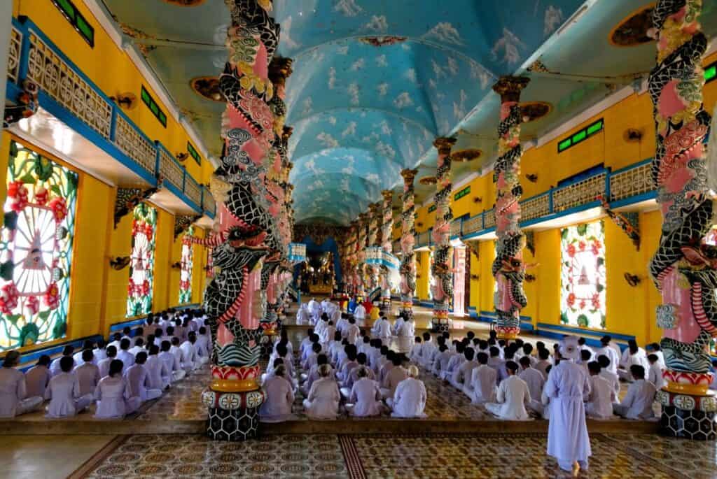 inside a temple with yellow walls and a blue ceiling with people dressed in white sitting in rows