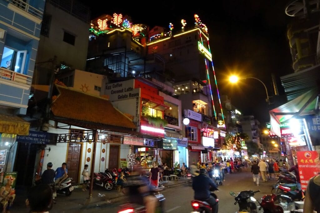 motorbikes riding on the street at night ouside a hotel lit with coloured lights